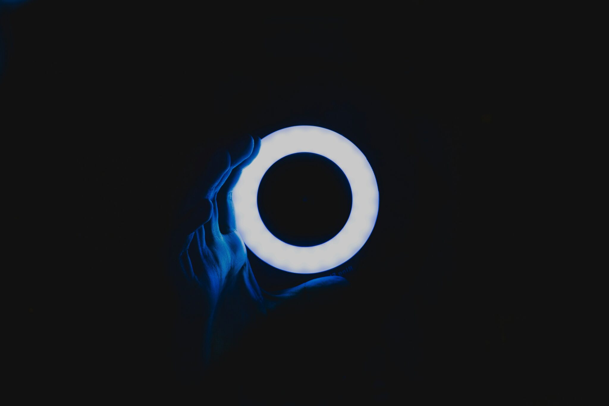  A hand holding a glowing blue circle against a black background, illustrating the concept of Circle to Search, a new visual search tool that lets you find what you're looking for by drawing a circle around it on your screen, compared to Google Lens, which is a visual search tool that lets you search for information about an object by taking a picture of it.